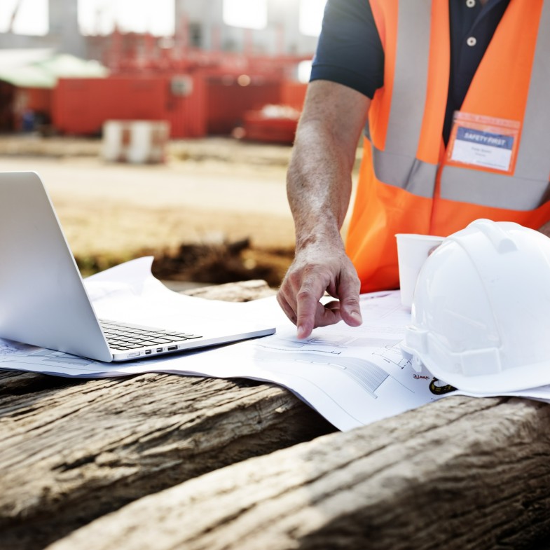 A construction worker planning using blue print and laptop in a construction site